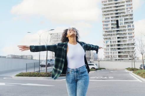 Happy young woman with arms outstretched enjoying on parking lot - MEUF08958
