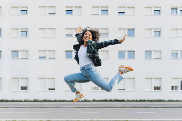 Fröhliche junge Frau springt vor einem Gebäude - MEUF08964
