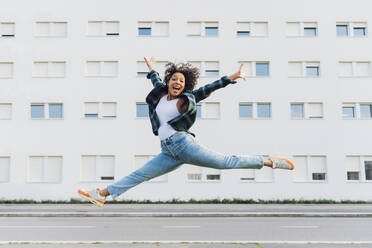 Fröhliche Frau springt vor einem Gebäude - MEUF08965