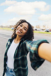 Eine fröhliche junge Frau nimmt ein Selbstporträt auf, während sie auf einer Straße steht - MEUF08972