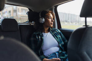 Nachdenkliche Frau trägt Bluetooth-Kopfhörer im Auto - MEUF08992