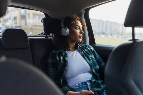 Thoughtful woman wearing bluetooth headphones in car - MEUF08992