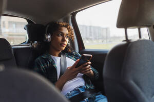 Nachdenkliche Frau mit Smartphone im Auto sitzend - MEUF08994
