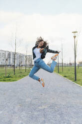 Cheerful young woman jumping on footpath - MEUF08997