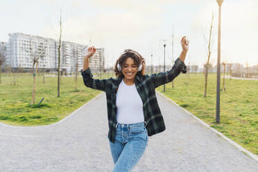 Happy woman wearing wireless headphones dancing on footpath - MEUF08999