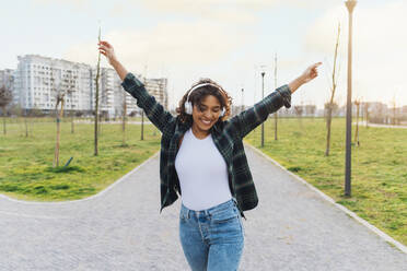 Happy young woman wearing wireless headphones dancing on footpath - MEUF09000