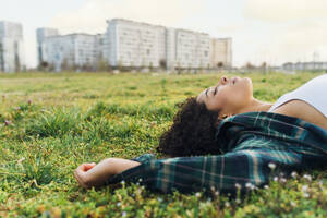 Junge Frau mit geschlossenen Augen entspannt im Gras bei Sonnenuntergang - MEUF09007