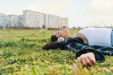 Junge Frau mit geschlossenen Augen entspannt und hört Musik im Gras bei Sonnenuntergang - MEUF09008
