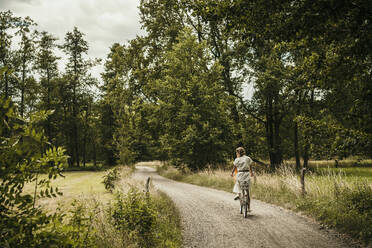 Woman riding bicycle on narrow dirt road - MJRF00927