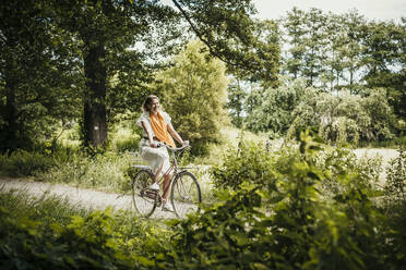 Woman riding bicycle amidst trees - MJRF00933