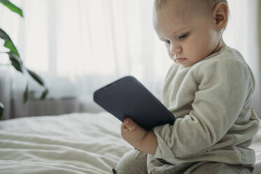 Kleiner Junge hält Smartphone auf dem Bett zu Hause - ANAF01113