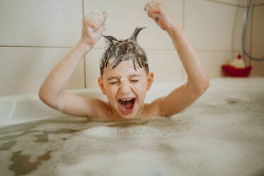 Verspielter Junge mit aufgestecktem Haar, der in der Badewanne schreit - ANAF01120