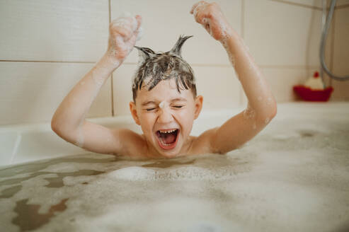 Verspielter Junge mit aufgestecktem Haar, der in der Badewanne schreit - ANAF01120