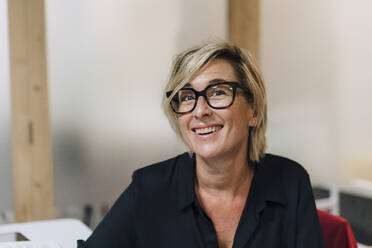 Happy businesswoman wearing eyeglasses at office - JOSEF17819