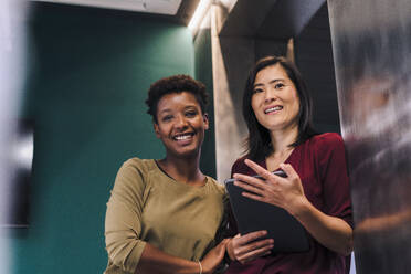 Happy businesswomen standing with tablet PC in office - JOSEF17878