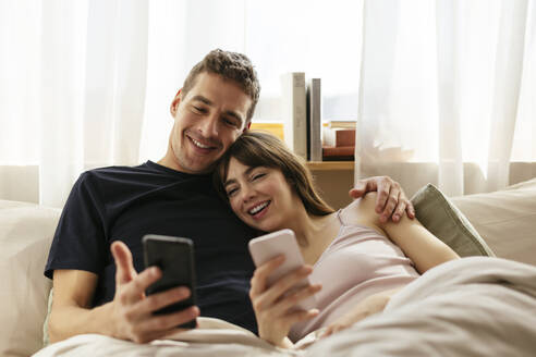 Glückliches Paar mit Smartphones, das sich zu Hause auf dem Bett entspannt - EBSF03002