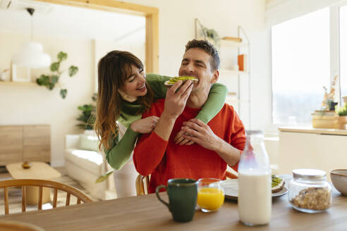 Happy woman with arm around man having breakfast at home - EBSF03015
