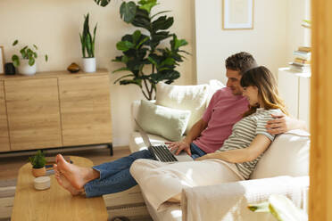 Freund mit Arm um Freundin mit Laptop auf Sofa im Wohnzimmer - EBSF03038