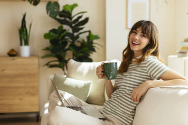 Happy woman with bangs holding coffee cup at home - EBSF03041