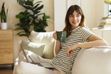 Thoughtful woman with coffee cup sitting on sofa - EBSF03042