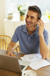 Happy freelancer wearing headset at table in home office - EBSF03056