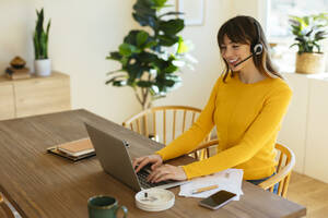 Glücklicher Freiberufler mit Headset und Laptop im Heimbüro - EBSF03058
