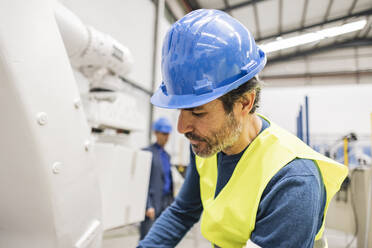 Ingenieur mit Schutzhelm bei der Arbeit an einem Roboterarm - JCCMF09935