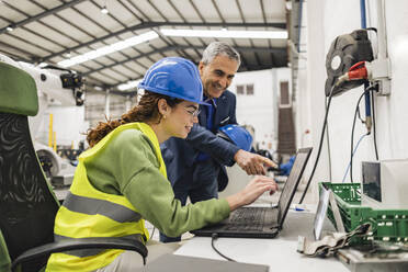 Glücklicher Geschäftsmann diskutiert mit einem Kollegen über einem Laptop in einer Fabrik - JCCMF09941