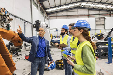 Mature engineer with colleagues having discussion over robotic arm - JCCMF09947