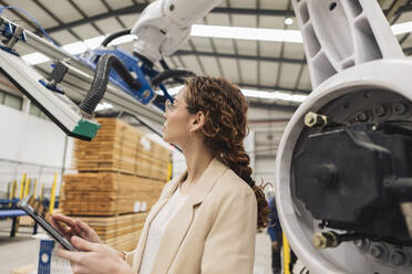 Junger Ingenieur mit Tablet-PC bei der Untersuchung eines Roboterarms in einer Fabrik - JCCMF09989