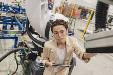 Junger Ingenieur mit Brille bei der Untersuchung eines Roboterarms in der Industrie - JCCMF09992