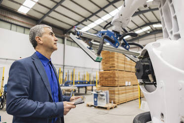 Älterer Geschäftsmann mit Tablet-PC, der einen Roboterarm in einer Fabrik untersucht - JCCMF09997