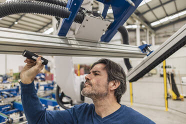 Ingenieur, der einen Roboterarm mit einer Taschenlampe in einer Fabrik untersucht - JCCMF10014
