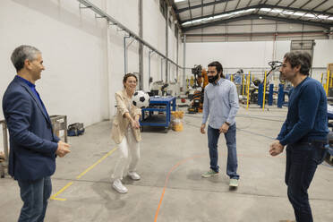 Happy engineers playing volleyball with soccer ball in industry - JCCMF10034