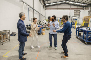 Happy engineers playing with soccer ball in industry - JCCMF10035