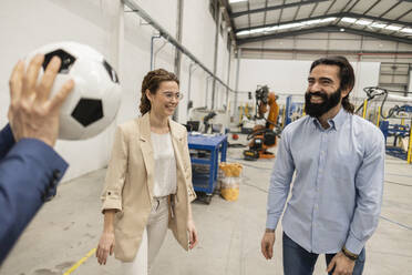 Happy engineers playing with soccer ball in factory - JCCMF10036