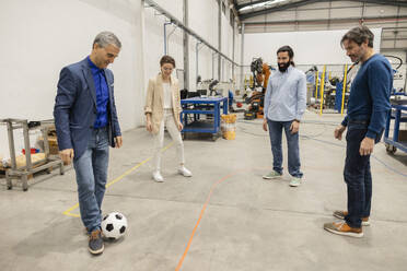 Engineers playing with soccer ball in factory - JCCMF10038