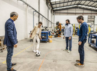 Business colleagues playing with soccer ball in factory - JCCMF10039