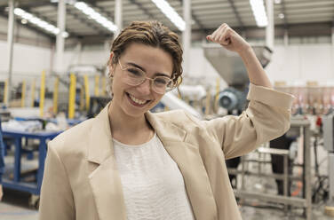 Happy businesswoman flexing muscles in industry - JCCMF10047