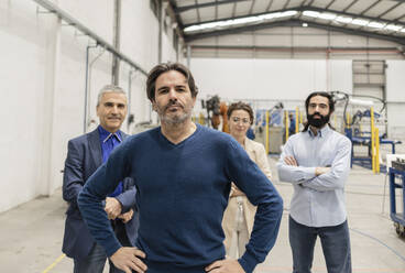 Engineer standing with hands on hip in front of colleagues at factory - JCCMF10051