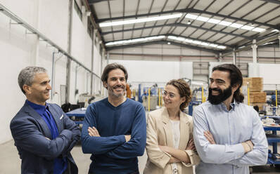 Glückliche Geschäftskollegen, die mit verschränkten Armen in der Industrie stehen - JCCMF10053