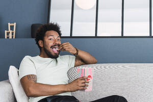 Mann isst Popcorn auf dem Sofa zu Hause - PNAF05116