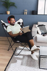 Mann beobachtet Tablet-PC auf einem Stuhl zu Hause sitzend - PNAF05127