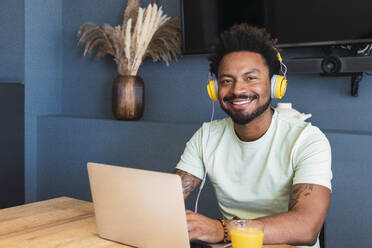 Lächelnder Mann mit Kopfhörern und Laptop, der zu Hause sitzt - PNAF05143