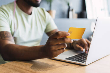 Man holding credit card by laptop in desk at home - PNAF05144