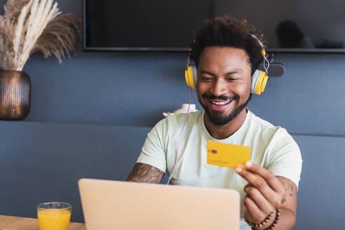 Happy man doing online shopping through credit card at home - PNAF05145