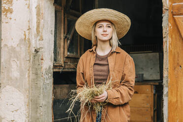 Farmer holding hay standing in barn - VSNF00637