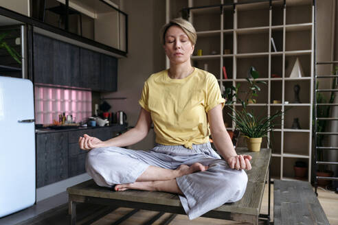 Frau mit geschlossenen Augen beim Üben der Lotus-Position zu Hause - VYF00946