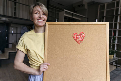 Glückliche Frau zeigt Pinnwand mit Herz-Emoji - VYF00948
