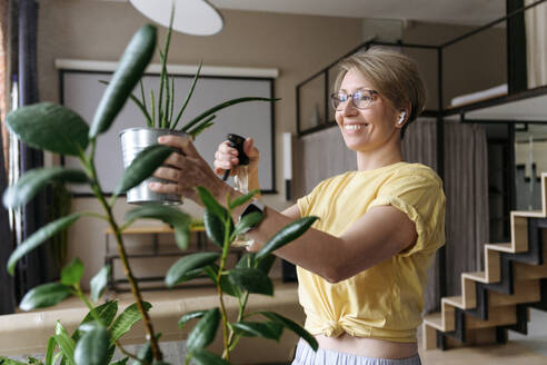Glückliche Frau, die Wasser auf eine Topfpflanze zu Hause sprüht - VYF00958